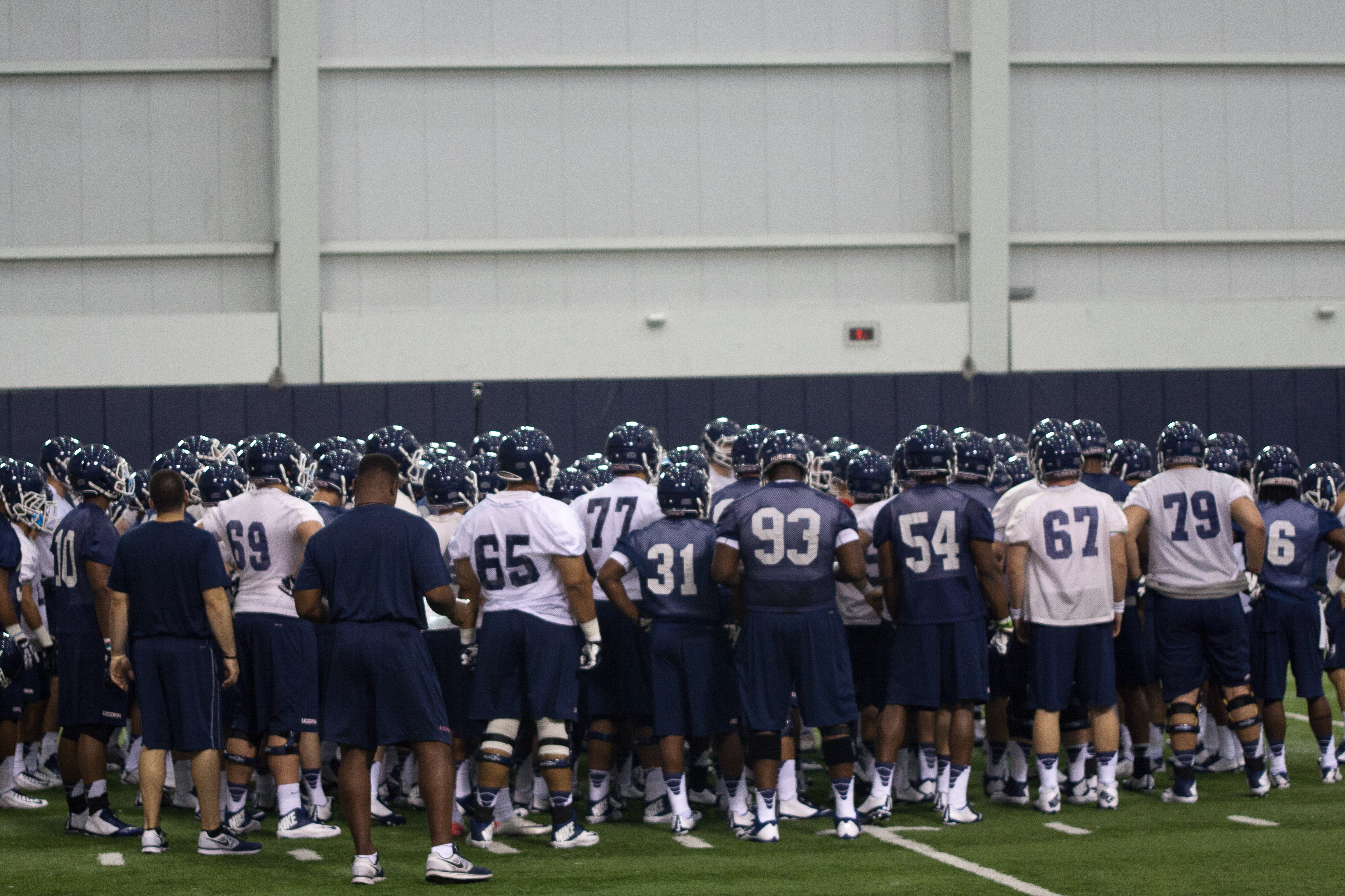 The UConn Football team gathers around head coach Bob Diaco before breaking into drills at the first practice of the 2014 season.